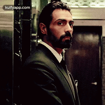 A Man In A Suit And Tie Is Standing In Front Of An Elevator Looking At The Camera . GIF