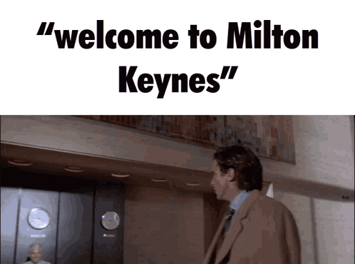 A Man In A Suit And Tie Is Standing In Front Of An Elevator With The Words " Welcome To Milton Keynes " Above Him GIF