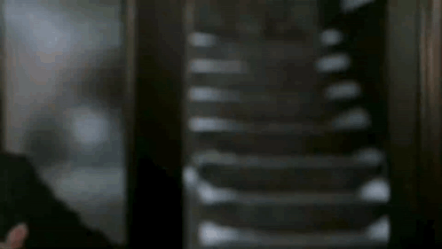 A Man In A Suit And Tie Is Standing In Front Of Stairs . GIF