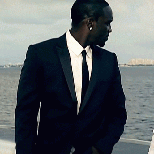 A Man In A Suit And Tie Is Standing In Front Of The Water GIF
