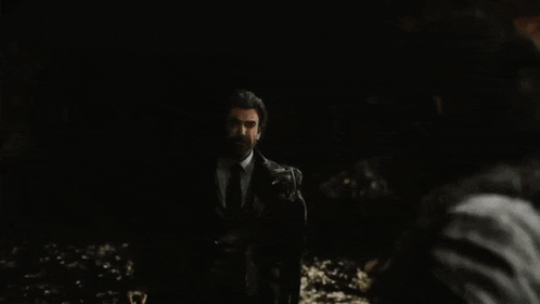 A Man In A Suit And Tie Is Standing In The Dark And Looking At Another Man . GIF