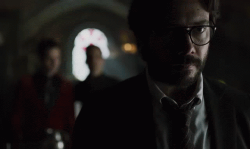 A Man In A Suit And Tie Is Standing In The Dark GIF