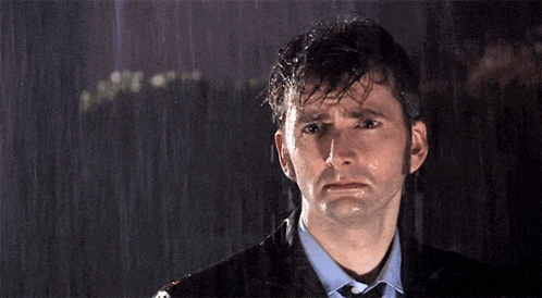 A Man In A Suit And Tie Is Standing In The Rain With His Eyes Closed GIF
