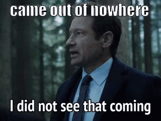 A Man In A Suit And Tie Is Standing In The Woods Looking At Something . GIF