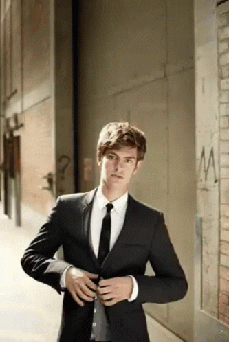 A Man In A Suit And Tie Is Standing Next To A Brick Wall . GIF