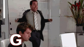 A Man In A Suit And Tie Is Standing Next To A Man In A Chair With The Letter G In Front Of Him GIF