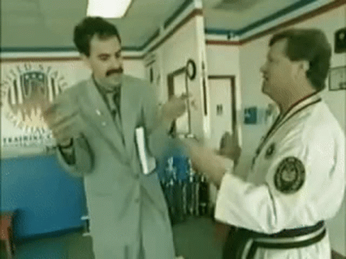 A Man In A Suit And Tie Is Standing Next To A Man In A Karate Uniform . GIF