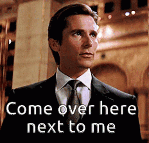 A Man In A Suit And Tie Is Standing Next To A Sign That Says Come Over Here Next To Me GIF
