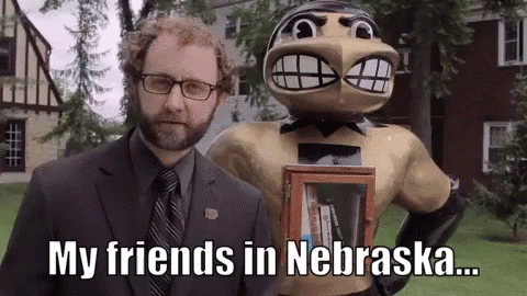 A Man In A Suit And Tie Is Standing Next To A Statue Of A Man With A Beard Holding A Book . GIF