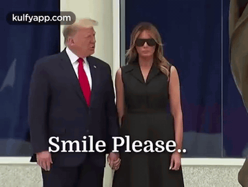 A Man In A Suit And Tie Is Standing Next To A Woman In A Black Dress Holding Hands . GIF