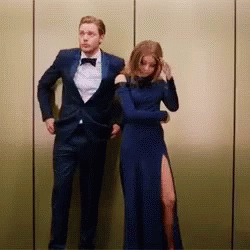 A Man In A Suit And Tie Is Standing Next To A Woman In A Blue Dress In An Elevator . GIF