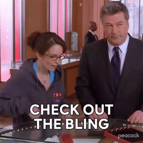 Man In Suit And Tie Next To Woman In Hoodie Saying Check Out The Bling GIF