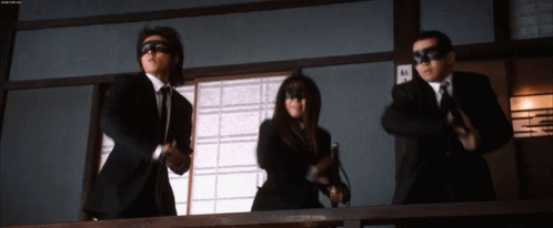 a man in a suit and tie is standing next to a woman in a mask and holding a gun