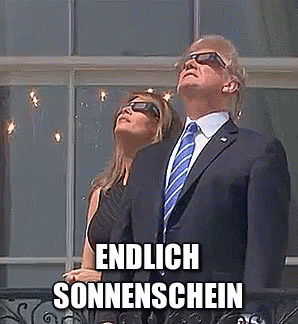 A Man In A Suit And Tie Is Standing Next To A Woman Wearing Sunglasses And Looking Up At The Sun . GIF