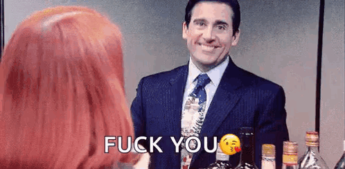 A Man In A Suit And Tie Is Standing Next To A Woman With Red Hair And Says `` Fuck You '' . GIF