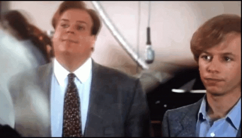 A Man In A Suit And Tie Is Standing Next To Another Man In A Blue Shirt GIF
