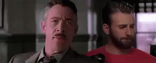 A Man In A Suit And Tie Is Standing Next To Another Man In A Red Shirt In A Room . GIF