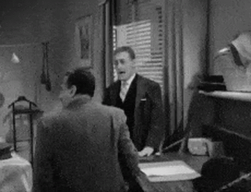 A Man In A Suit And Tie Is Standing Next To Another Man In A Room . GIF