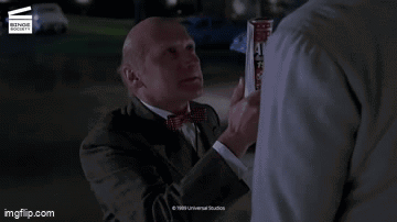 A Man In A Suit And Tie Is Standing Next To Another Man With The Words Slacker On The Screen GIF
