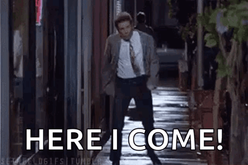 A Man In A Suit And Tie Is Standing On A Sidewalk With The Words `` Here I Come '' Written On It . GIF