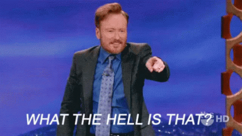 A Man In A Suit And Tie Is Standing On A Stage And Pointing At The Camera . GIF