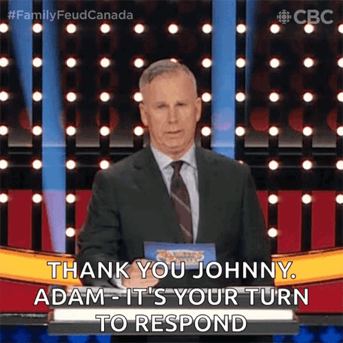 A Man In A Suit And Tie Is Standing On A Stage And Says Thank You Johnny Adam It 'S Your Turn To Respond GIF