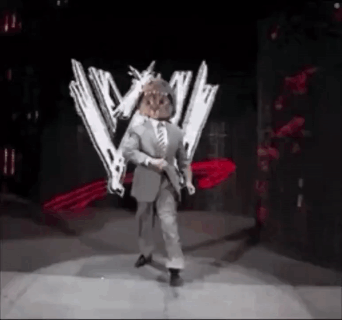 A Man In A Suit And Tie Is Standing On A Stage Holding Two Guns . GIF