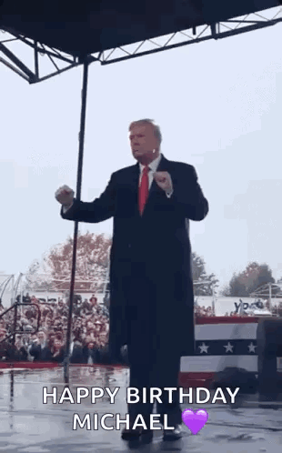 A Man In A Suit And Tie Is Standing On A Stage In Front Of A Crowd And Giving A Speech . GIF