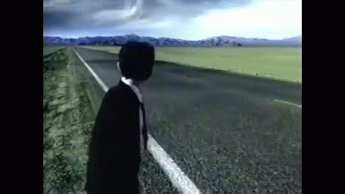 A Man In A Suit And Tie Is Standing On The Side Of A Highway . GIF