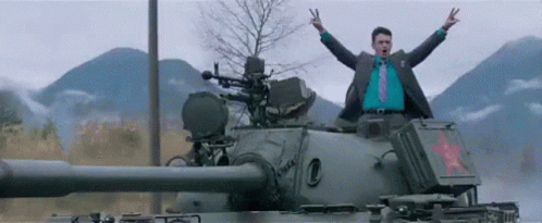 A Man In A Suit And Tie Is Standing On Top Of A Tank With His Arms In The Air GIF