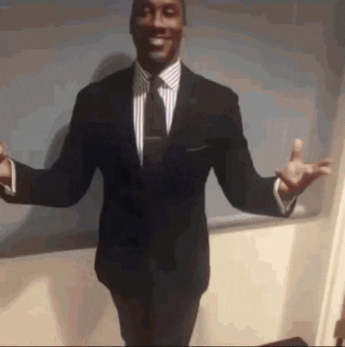 A Man In A Suit And Tie Is Standing With His Arms Outstretched And Smiling GIF