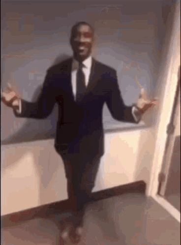 A Man In A Suit And Tie Is Standing With His Arms Outstretched In A Hallway . GIF