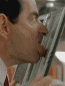 A Man In A Suit And Tie Is Sticking His Tongue Out While Eating Something . GIF