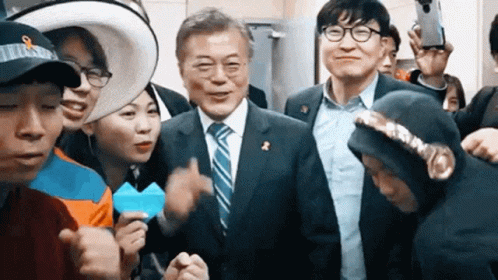 A Man In A Suit And Tie Is Surrounded By A Group Of People . GIF
