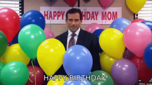 A Man In A Suit And Tie Is Surrounded By Balloons And A Sign That Says `` Happy Birthday Mom '' . GIF