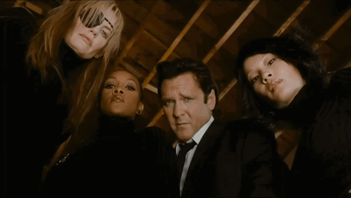 a man in a suit and tie is surrounded by three women in black