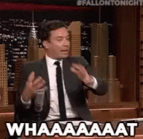 A Man In A Suit And Tie Is Talking Into A Microphone And Saying Whaaaaat GIF