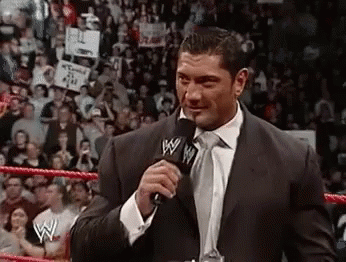 A Man In A Suit And Tie Is Talking Into A Microphone In Front Of A Crowd . GIF