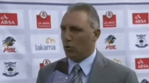 A Man In A Suit And Tie Is Talking Into A Microphone In Front Of A Wall With Logos For Absa Lakama And Psl GIF