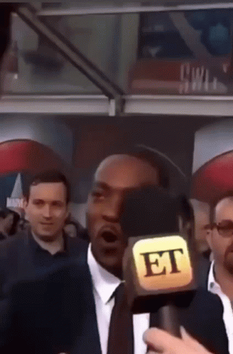 A Man In A Suit And Tie Is Talking Into A Microphone That Says Et GIF