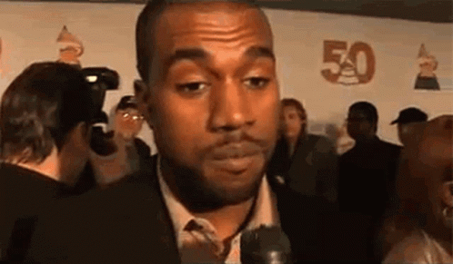 A Man In A Suit And Tie Is Talking Into A Microphone While Standing In Front Of A Crowd . GIF