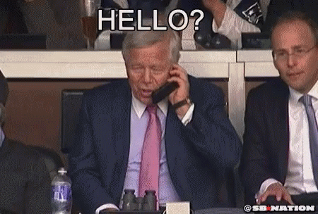 A Man In A Suit And Tie Is Talking On A Cell Phone While Another Man Says Hello GIF