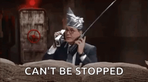 A Man In A Suit And Tie Is Talking On A Cell Phone While Wearing An Aluminum Foil Hat . GIF