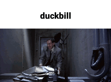 A Man In A Suit And Tie Is Talking On A Phone In A Dark Room With The Word Duckbill Above Him GIF