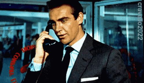 A Man In A Suit And Tie Is Talking On A Phone In Front Of A Sign That Says Chrome GIF