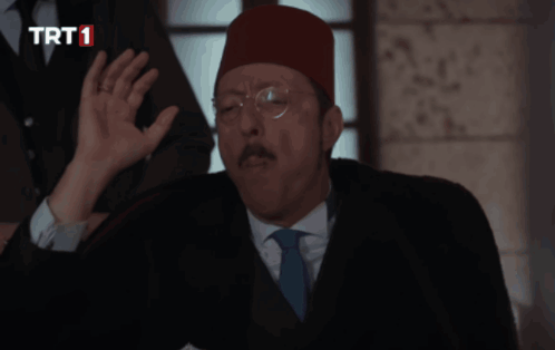 A Man In A Suit And Tie Is Talking On A Phone With A Trt1 Logo In The Corner GIF