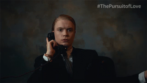 A Man In A Suit And Tie Is Talking On A Phone With #Thepursuitoflove Written On The Bottom Right GIF