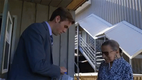 A Man In A Suit And Tie Is Talking To A Woman In A Blue And White Dress GIF