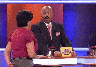 A Man In A Suit And Tie Is Talking To A Woman In A Red Shirt On A Game Show GIF