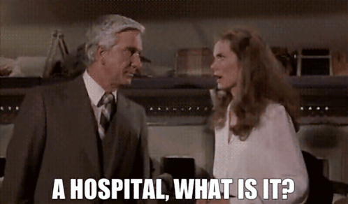A Man In A Suit And Tie Is Talking To A Woman In A White Shirt Who Says " A Hospital What Is It ? " GIF